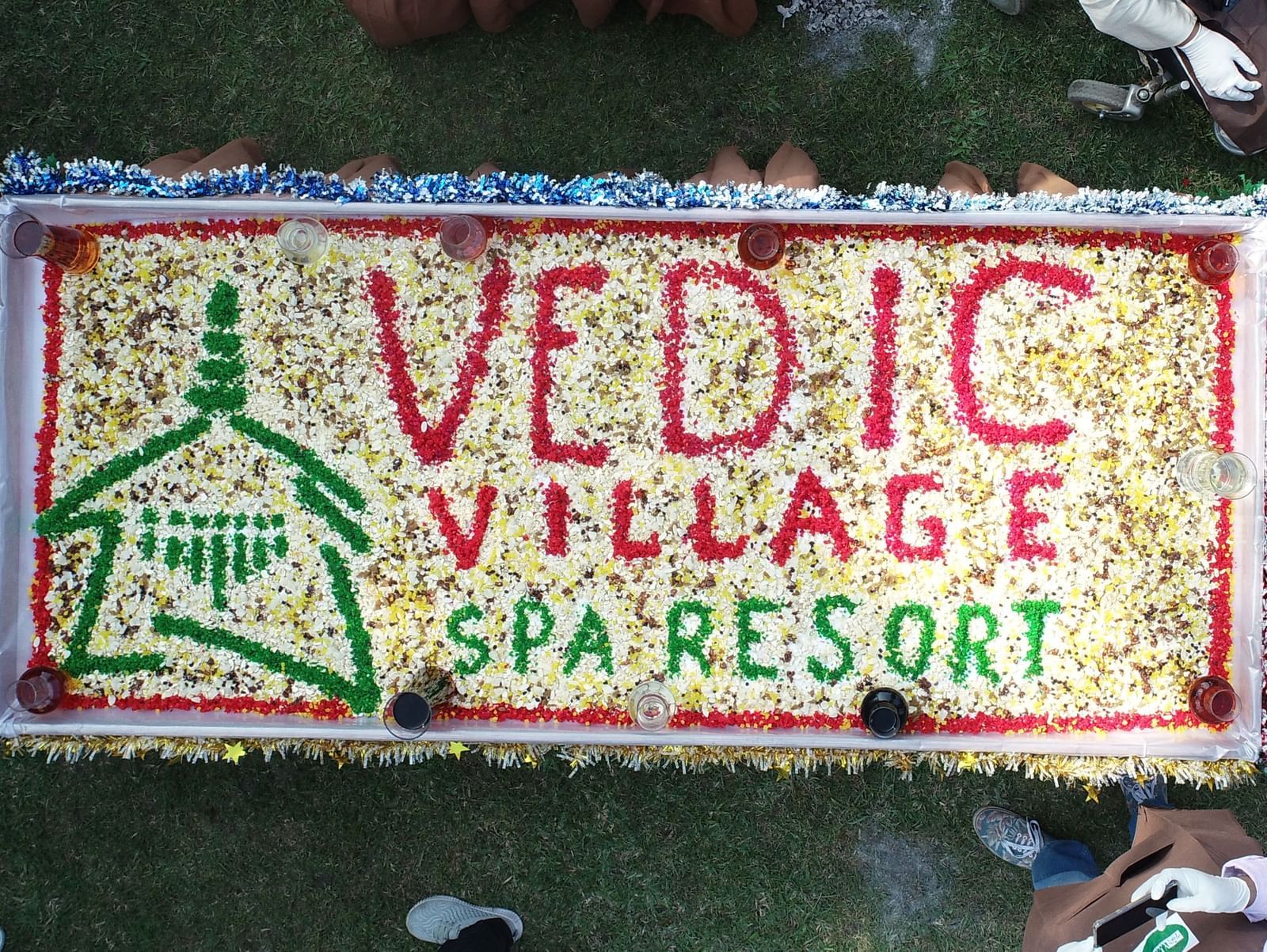An aerial view shows people gathered around a large 'Vedic Village Spa and Resort' sign made on the cake