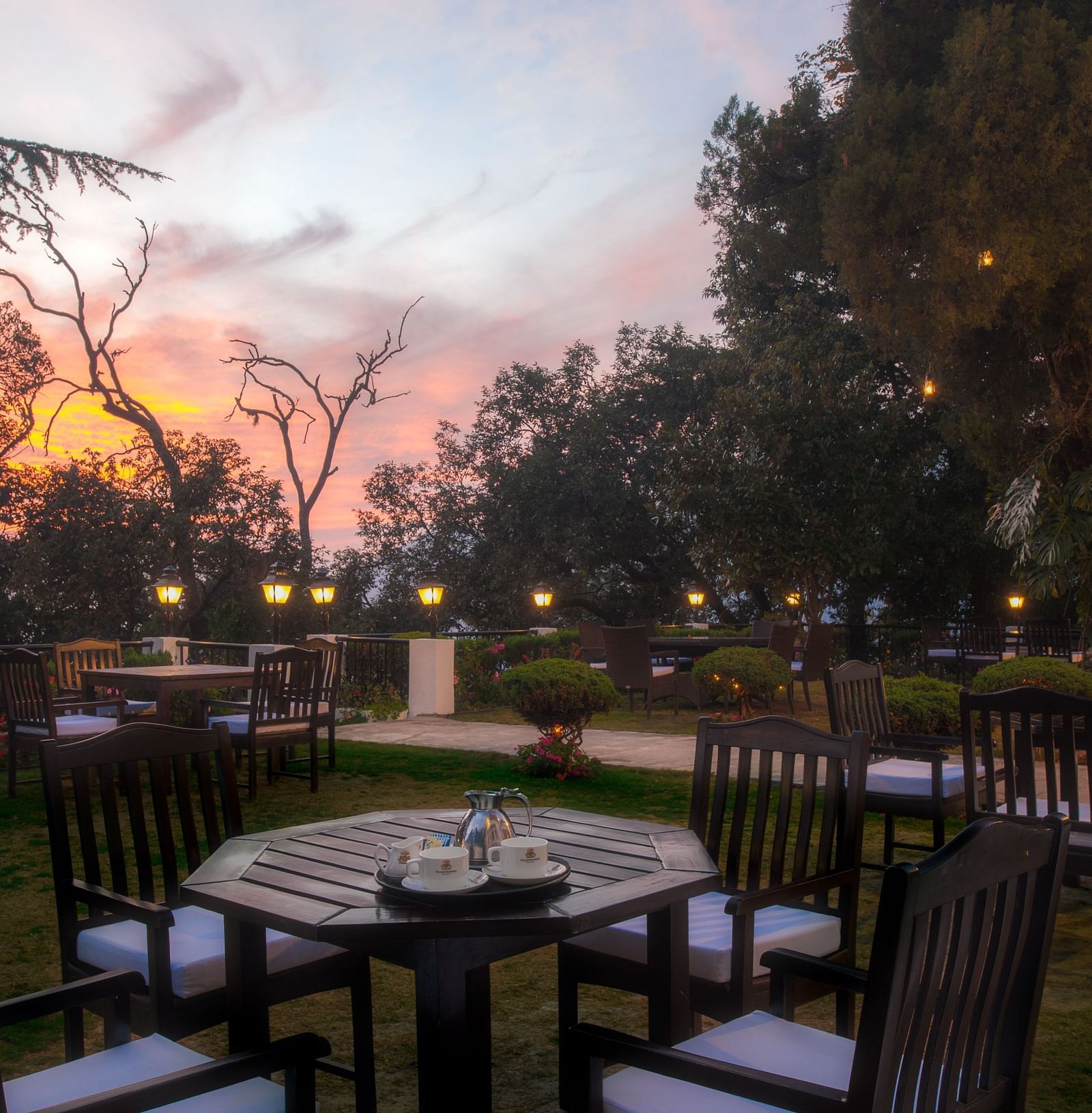 outdoor dining area with tables and chairs with the backdrop of a sunset at the Claridges Nabha Residence, Mussoorie