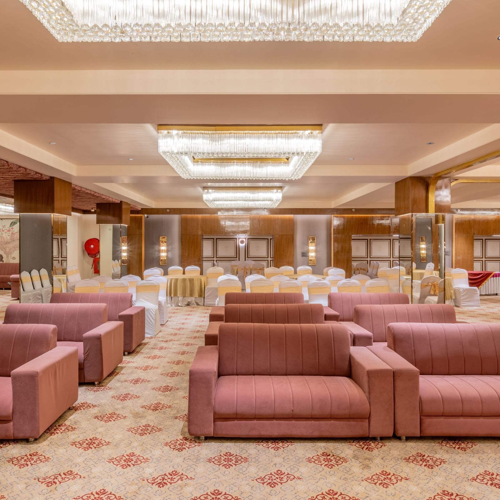 Maroon sofas arranged in a banquet hall with bright ceiling lights above at Hotel Highway King, Jaipur.
