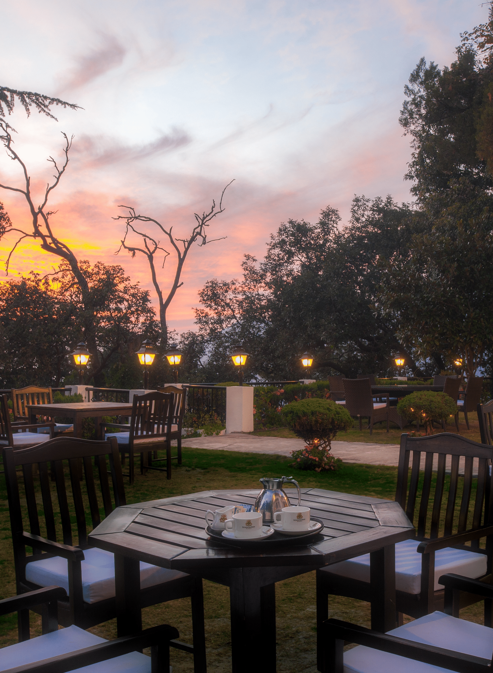 outdoor dining area with tables and chairs with the backdrop of a sunset at the Claridges Nabha Residence, Mussoorie