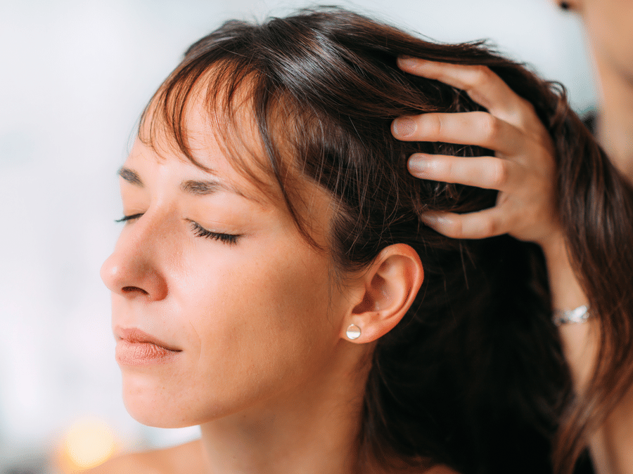 Woman receiving scalp massage with eyes closed in a spa environment.