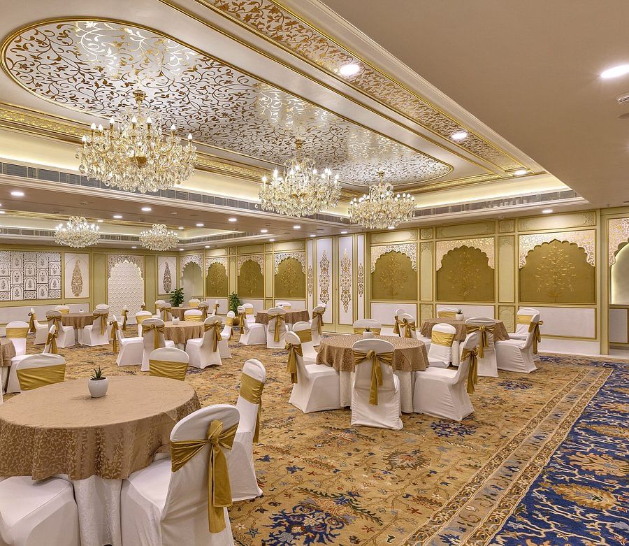 Lavish ballroom with ornate ceiling, multiple chandeliers, and round tables with white and gold accents - Heritage Village Resorts & Spa.