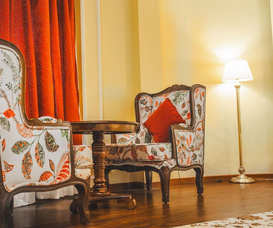 Two wooden sofa chairs with comfy cushions facing each other with a wooden teapoy in the middle, at the Super deluxe room at The Garden Ananta Elite.