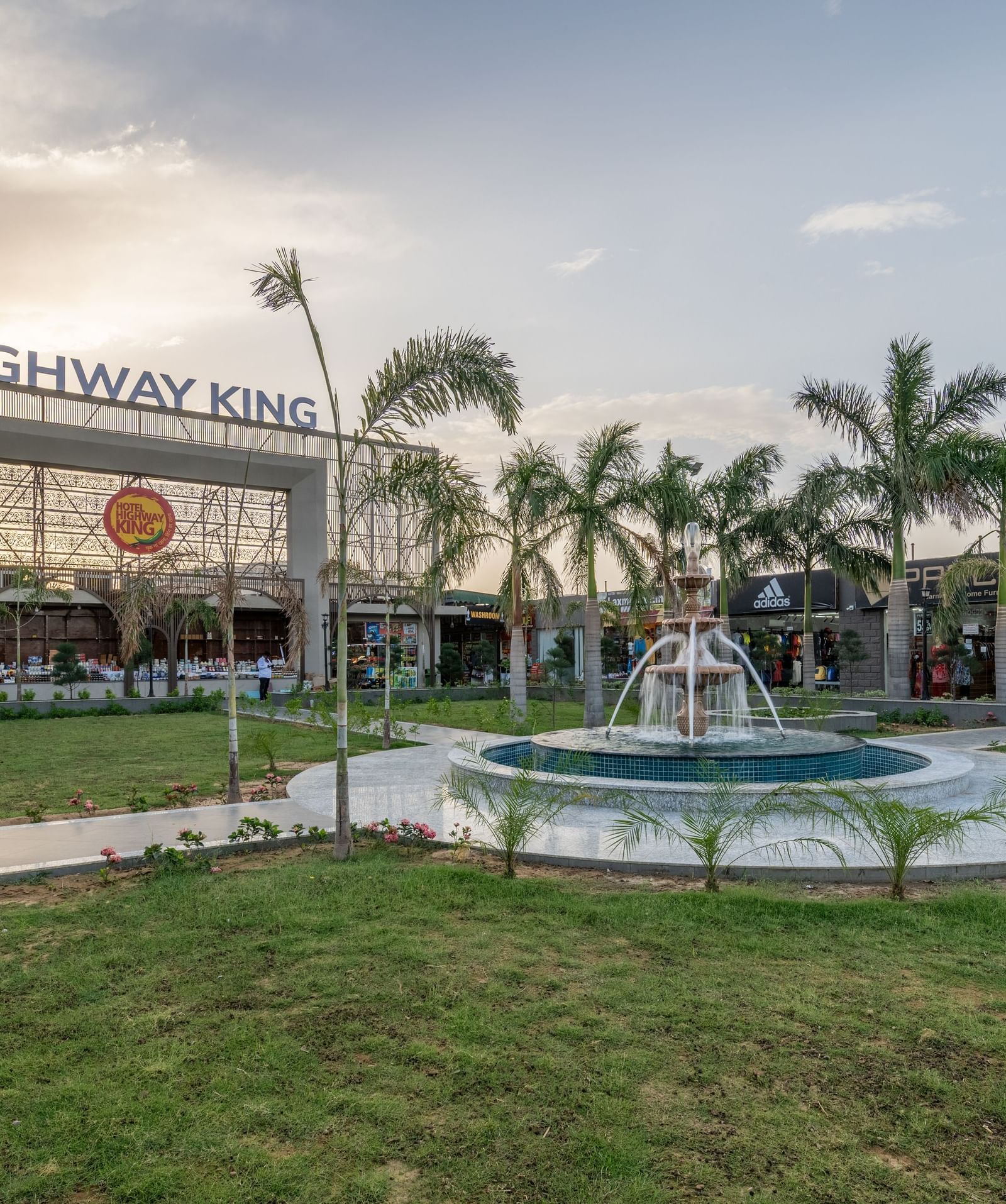 Exterior view of Hotel Highway King, Neelka against a cloudy sky, featuring the lawn area with a water fountain.