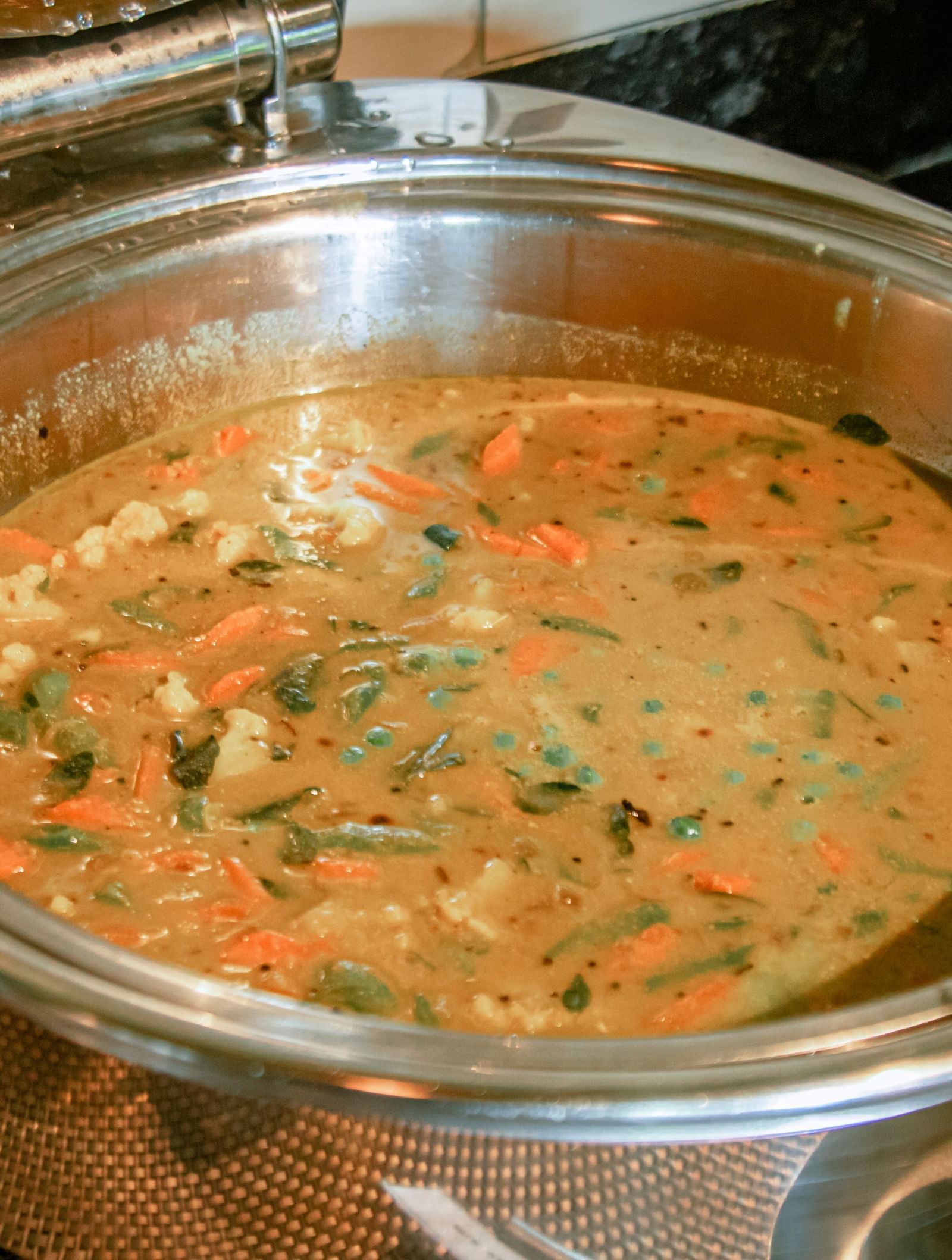 Close-up of a chafing dish containing a creamy vegetable curry garnished with herbs at Fireflies Resorts, Kabini.