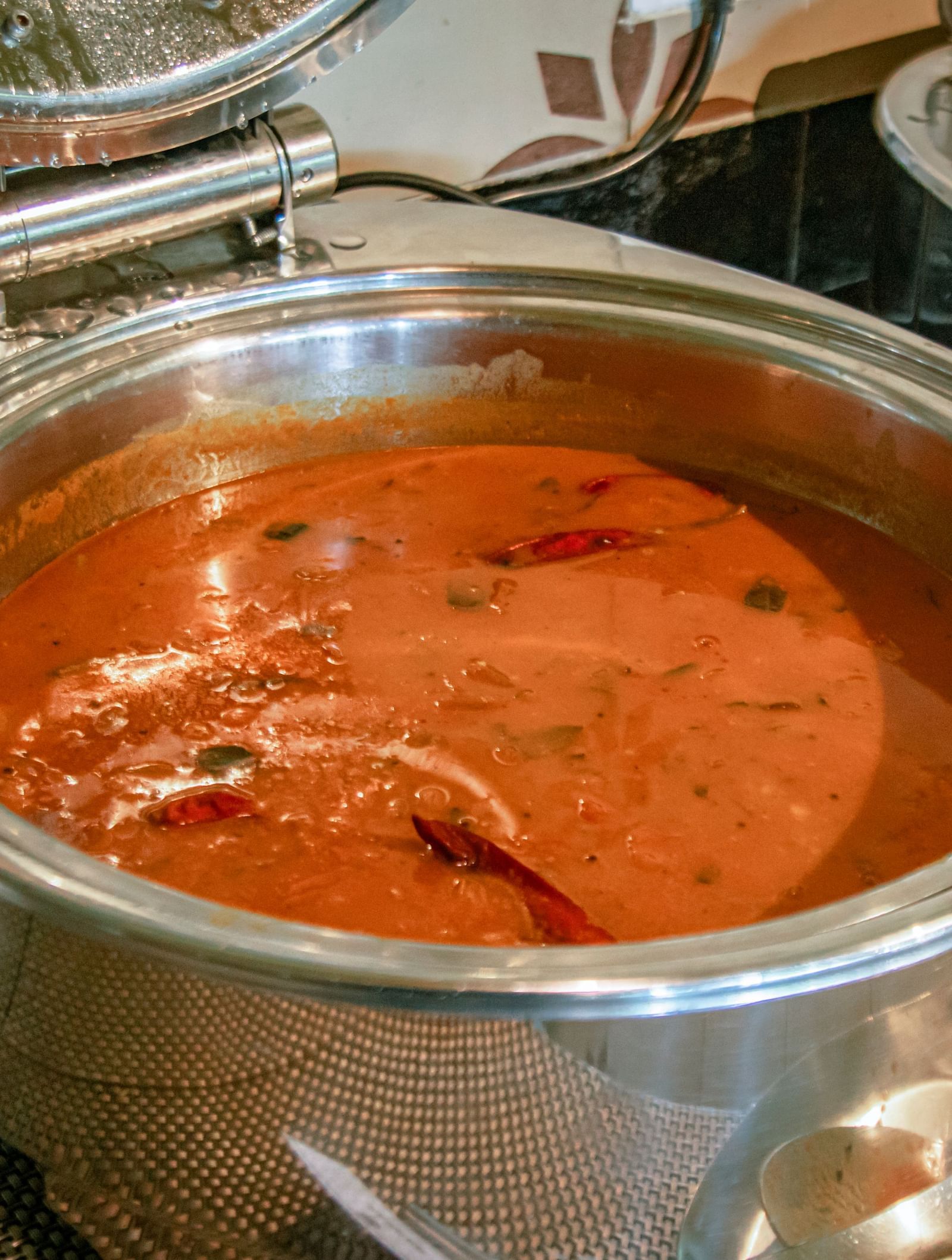 Close-up of a hot dish in a round chafing dish filled with red curry at Fireflies Resorts, Kabini.