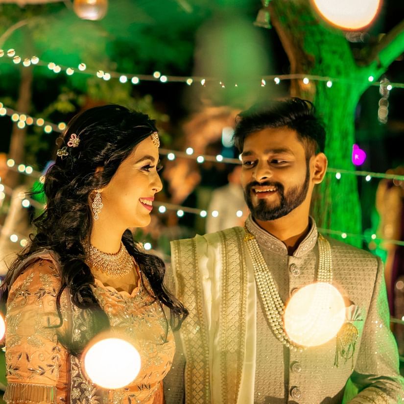 a couple posing with fairy lights lit at the back