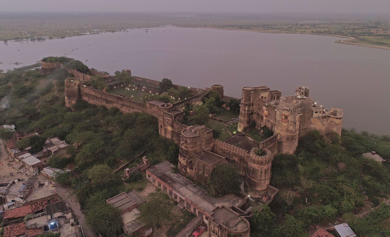 An aerial view of a ruined stone fortress perched on a hill overlooking a large body of water- Shahpura Bagh.