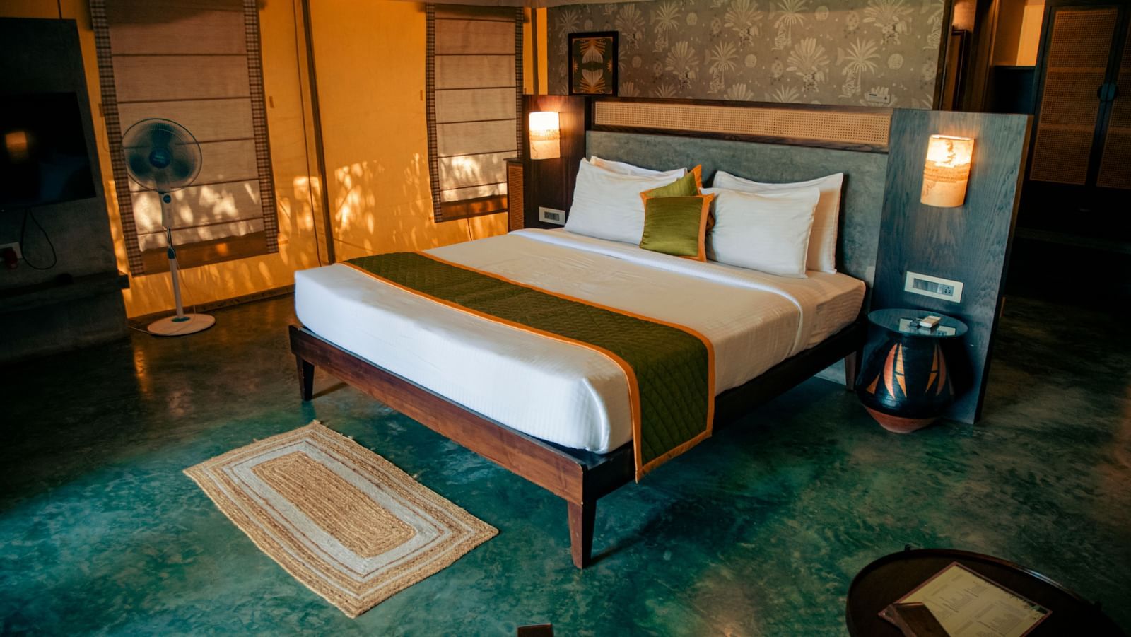 Bedroom with green flooring, king size bed, bedside lamps, and rug at Fireflies Resorts, Kabini.