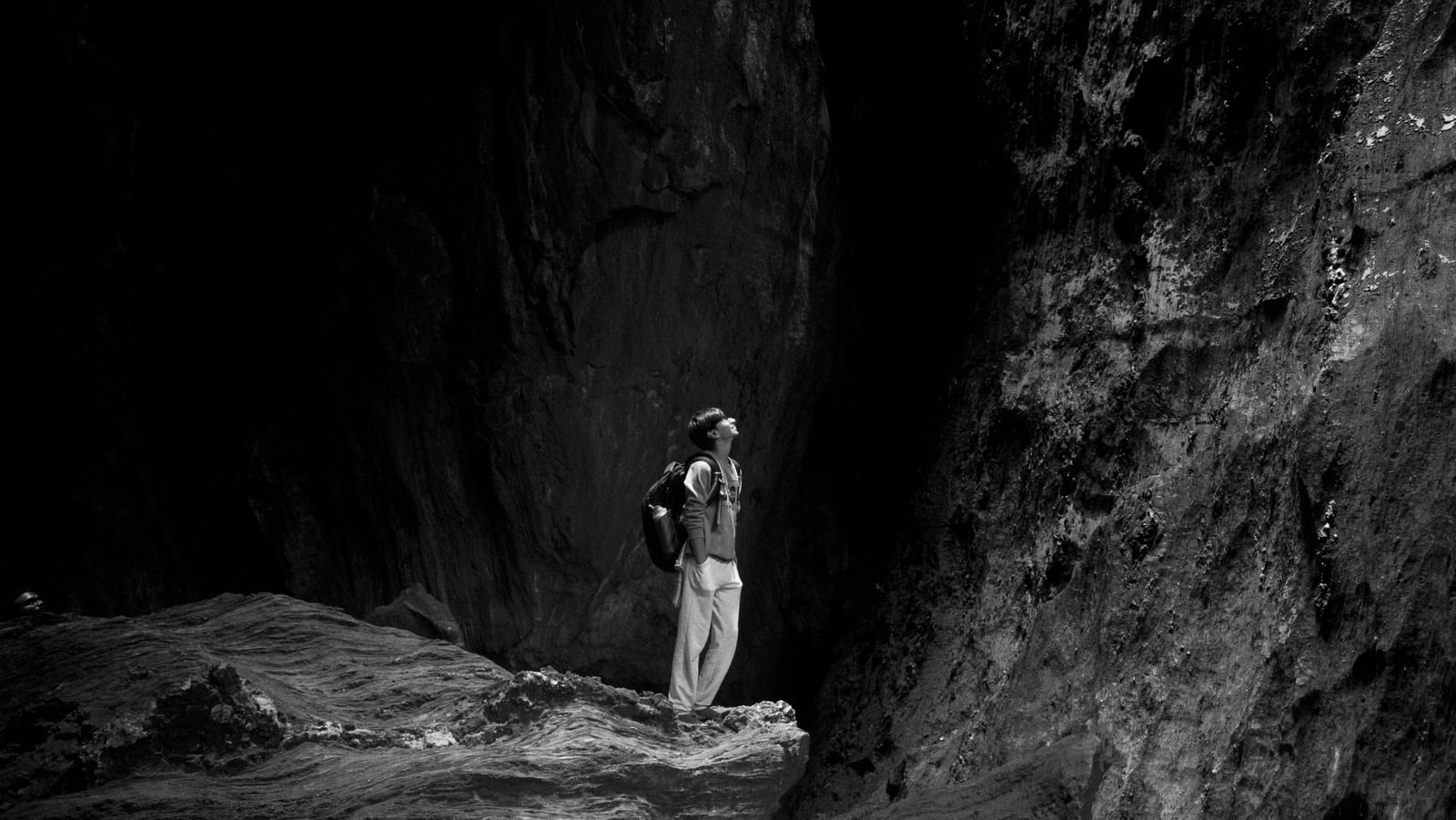 A person standing on rocky terrain, surrounded by towering natural rock formations, looking upwards in a contemplative pose.