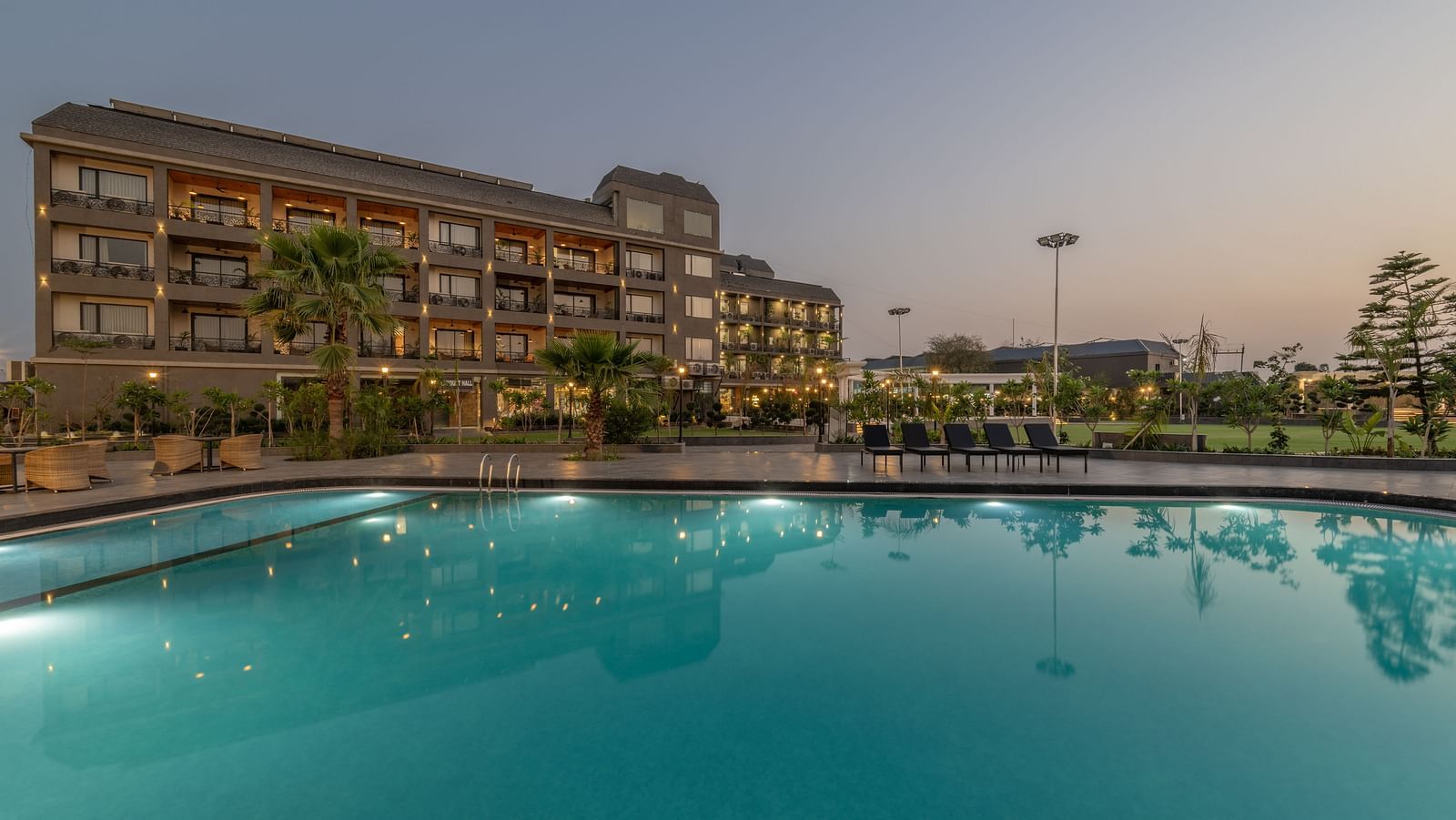 Swimming pool area at Hotel Highway King, Bagru, with loungers, landscaped surroundings, and the main building in view.