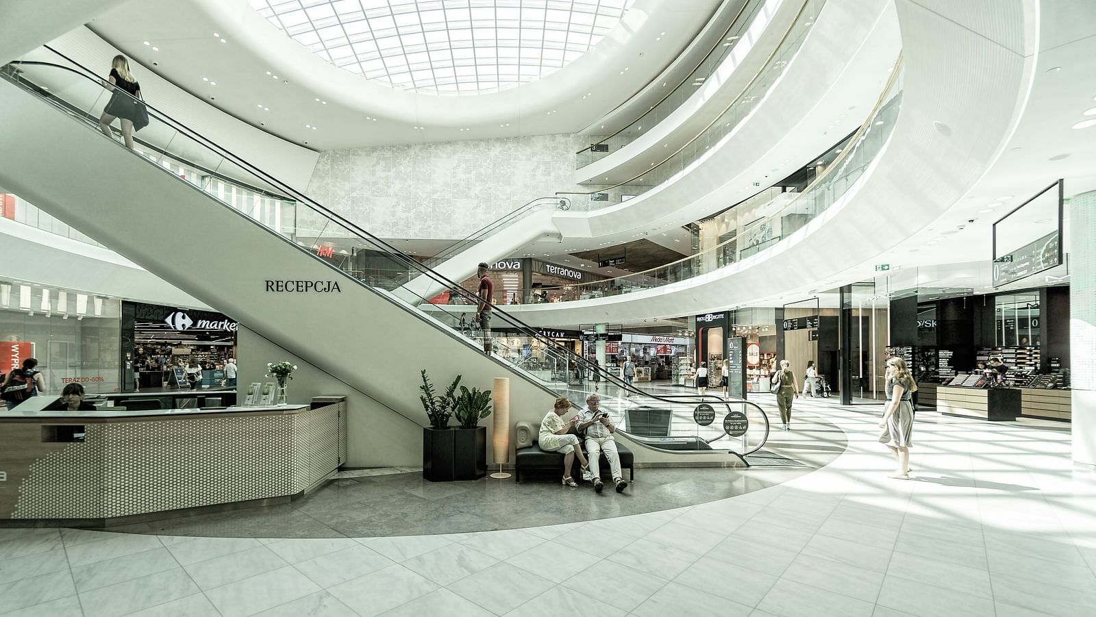 An overview of a mall with people sitting near the escalators and passing by it.