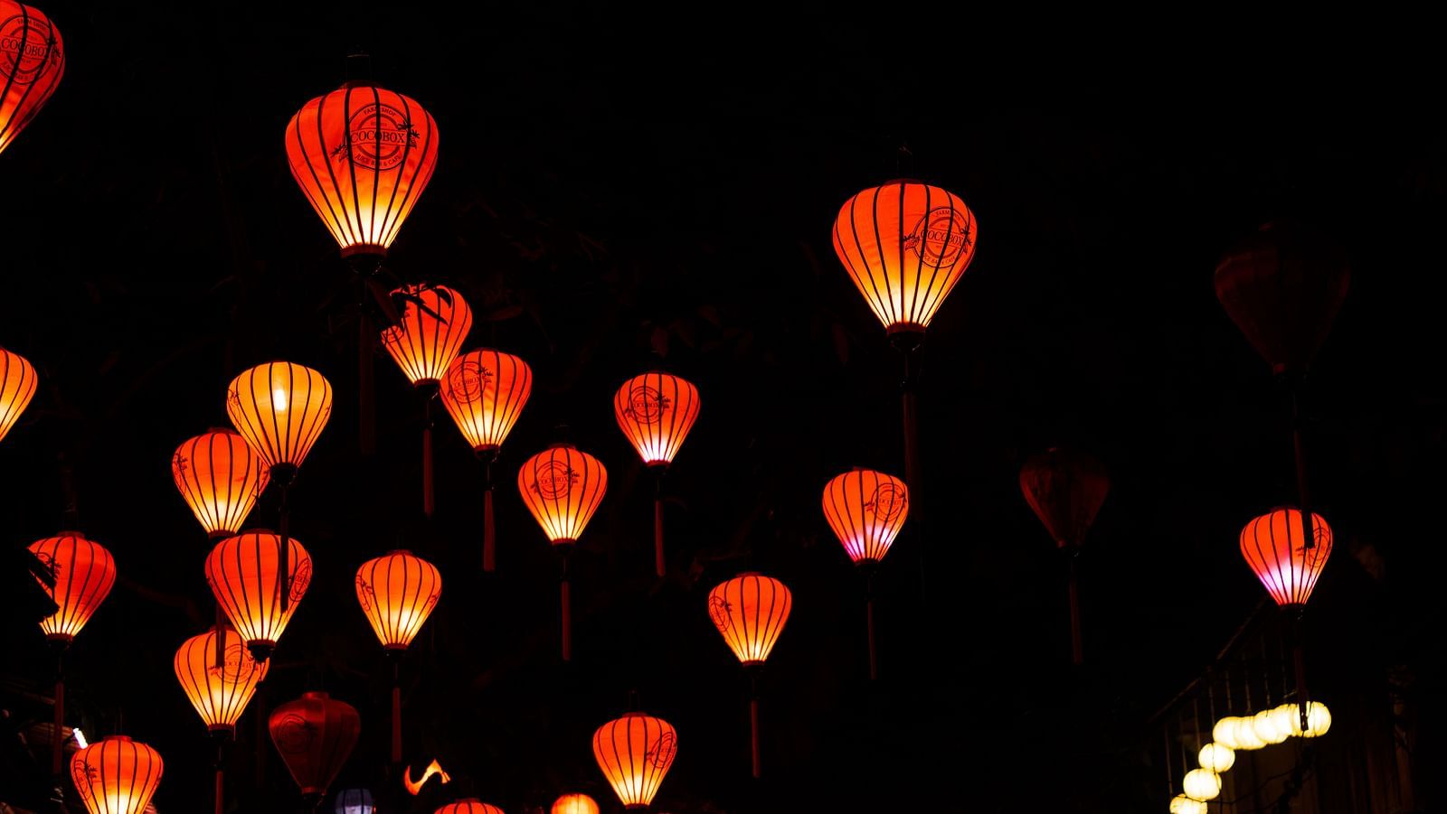 Many Handmade lanterns hung on a thread in a row in the night with the fire on inside
