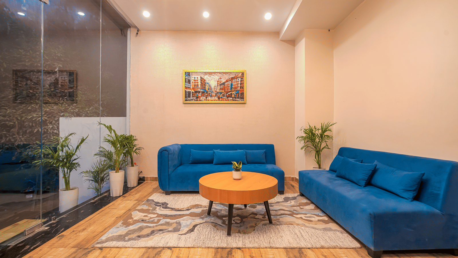 A lounge area at Perfectstayz Premium Varanasi, featuring 2 blue sofa, an artistic wall frame, a round table, and a rug.
