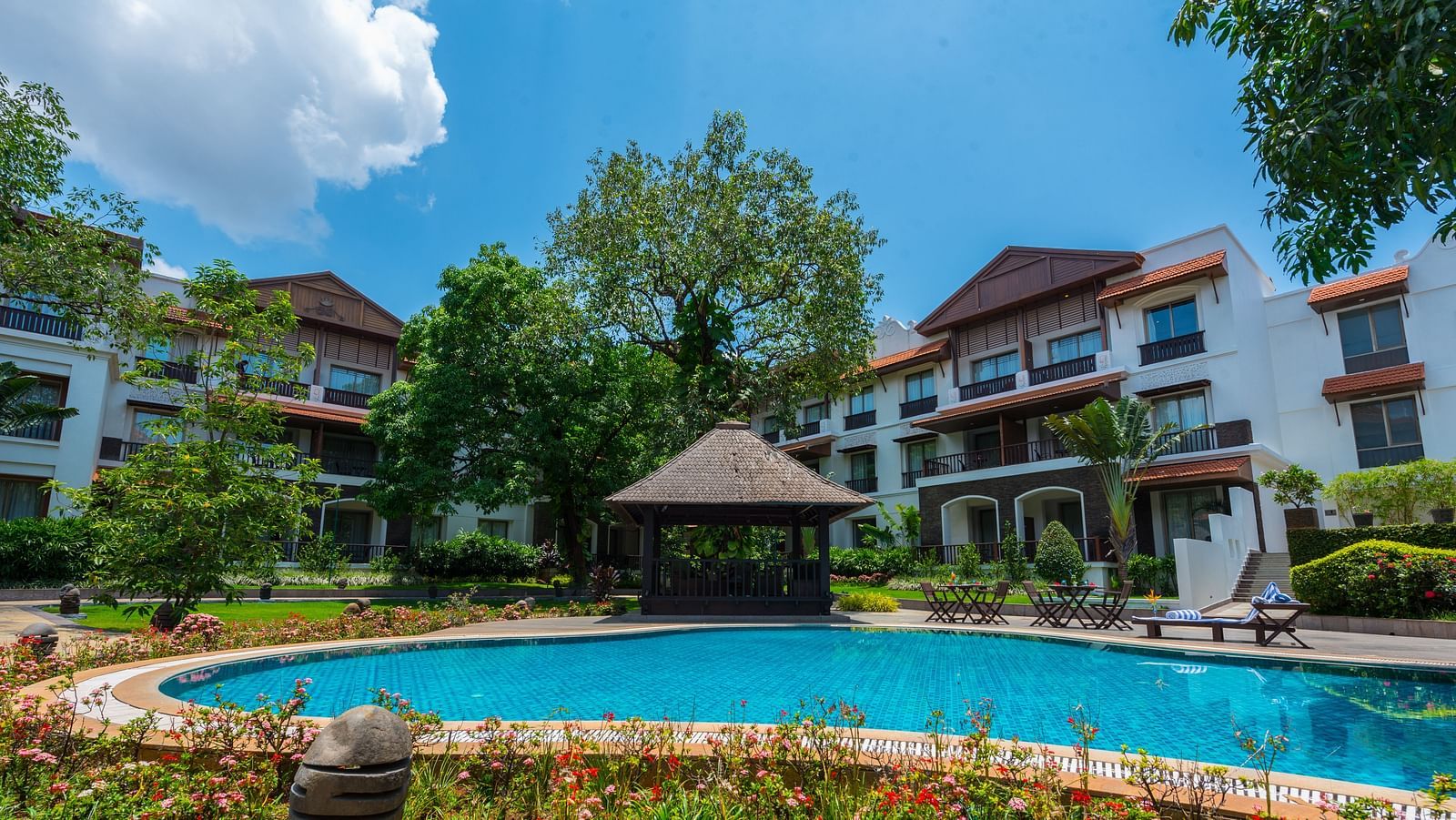 The facade of Rhythm Lonavala with a pool at the foreground and trees next to the buildings. 