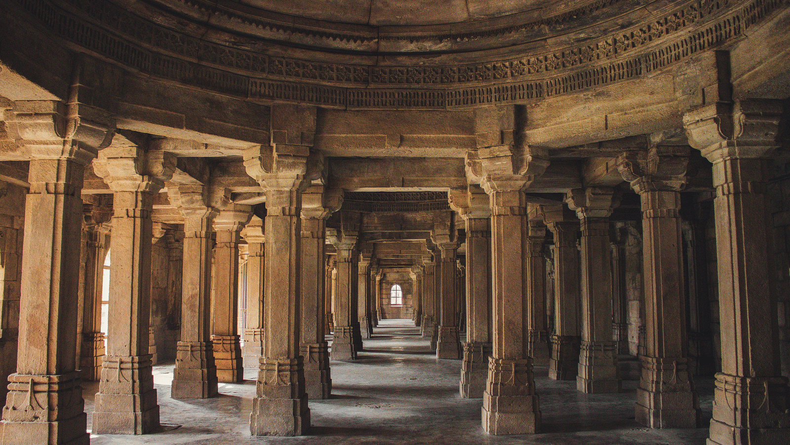 Multiple beams support inside a temple with the sun shining inside.