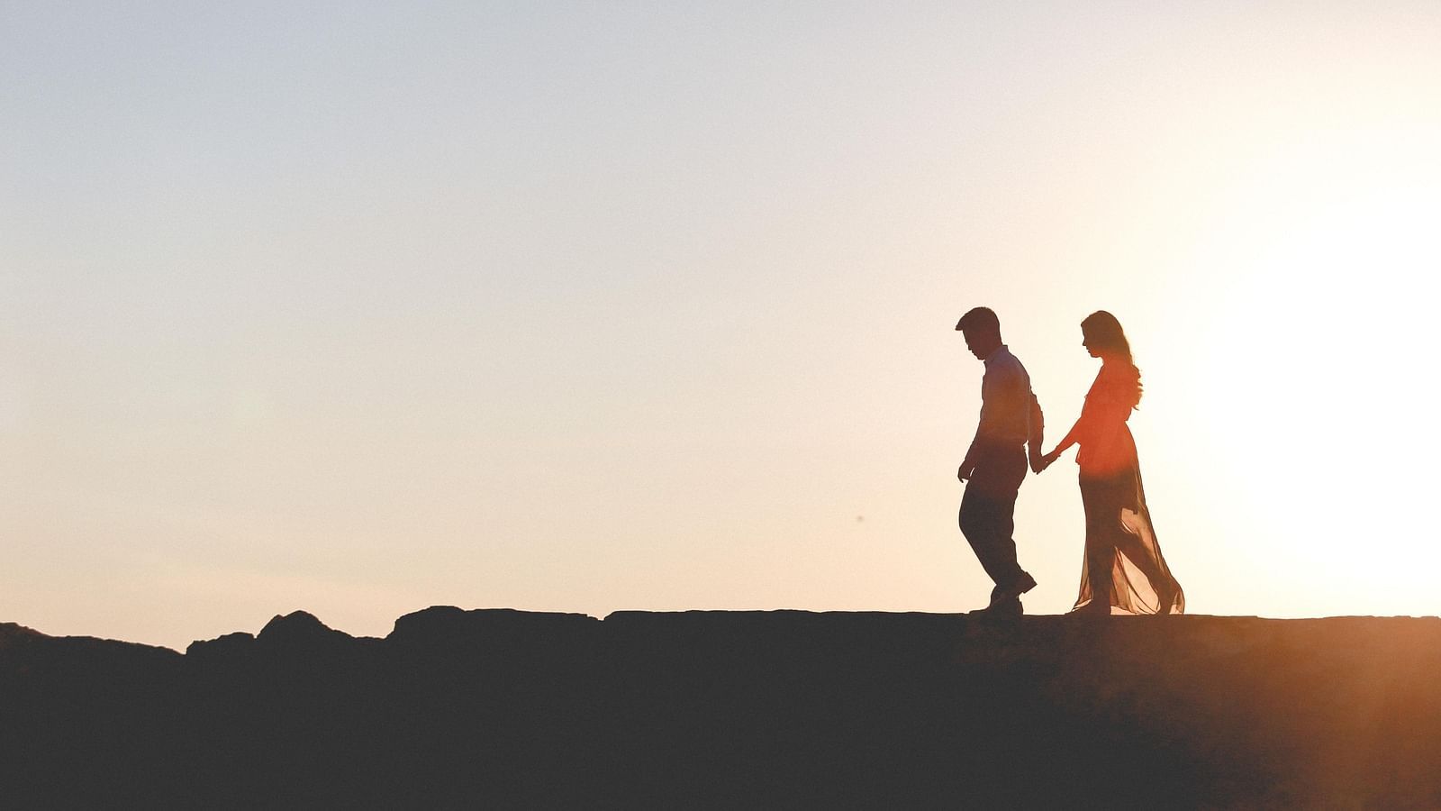 a Couple walking on a ledge with the sun setting in the background - Rhythm Kumarakom