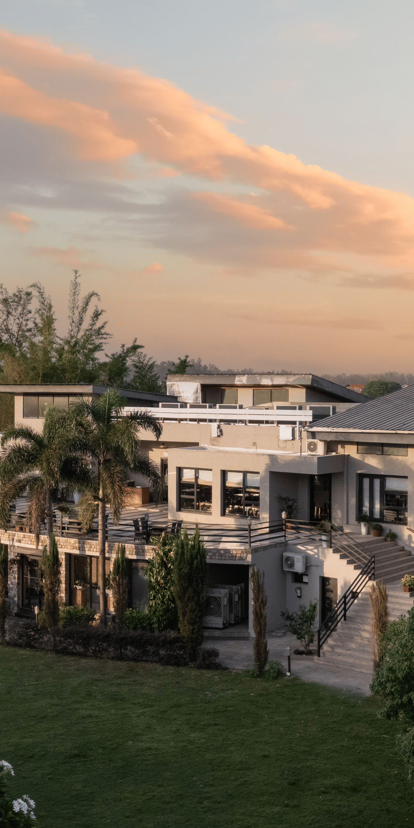 Resort building in the distance, surrounded by green lawns and trees at sunset at The Golden Tusk, Jim Corbett