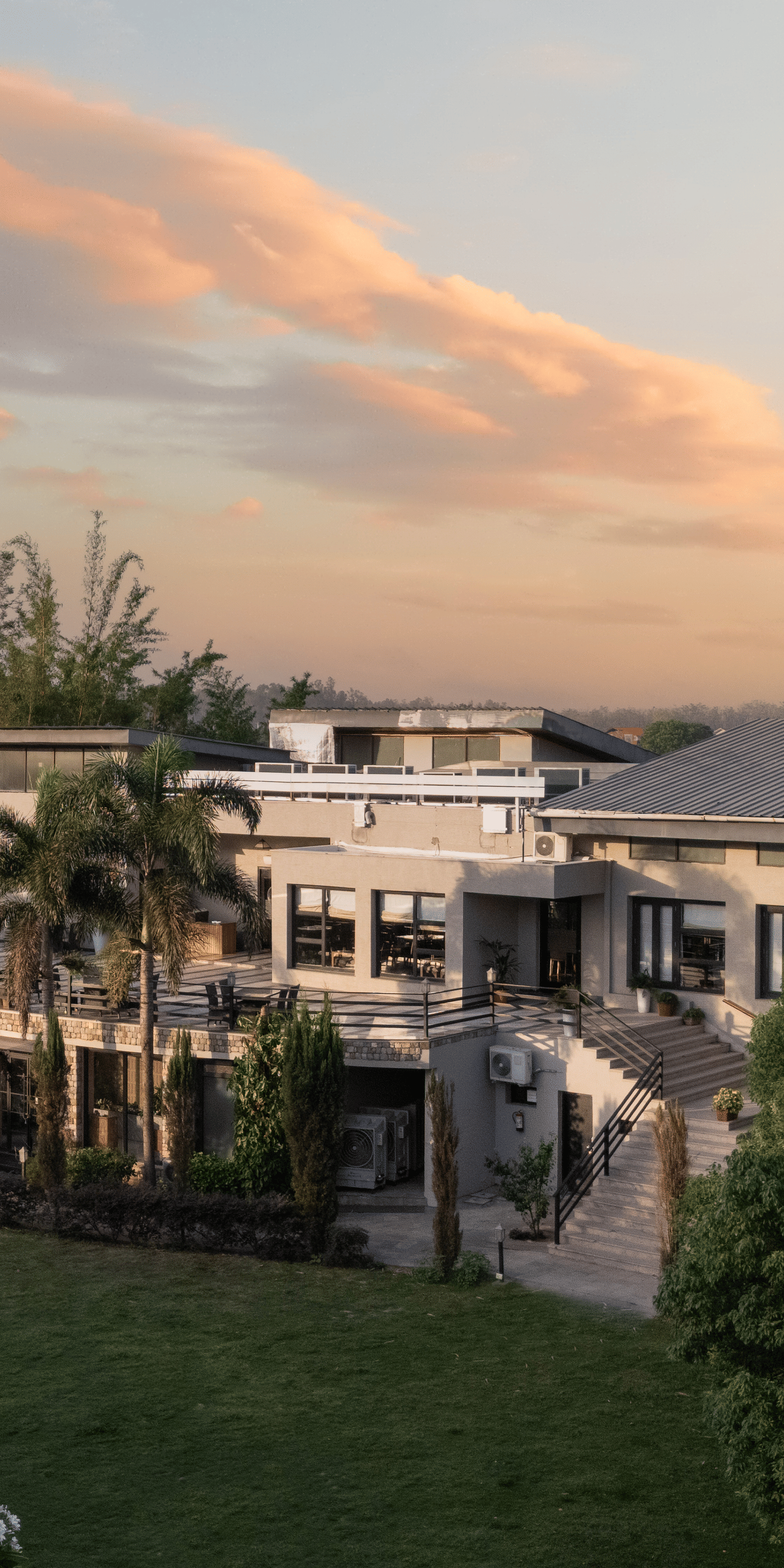Resort building in the distance, surrounded by green lawns and trees at sunset at The Golden Tusk, Jim Corbett