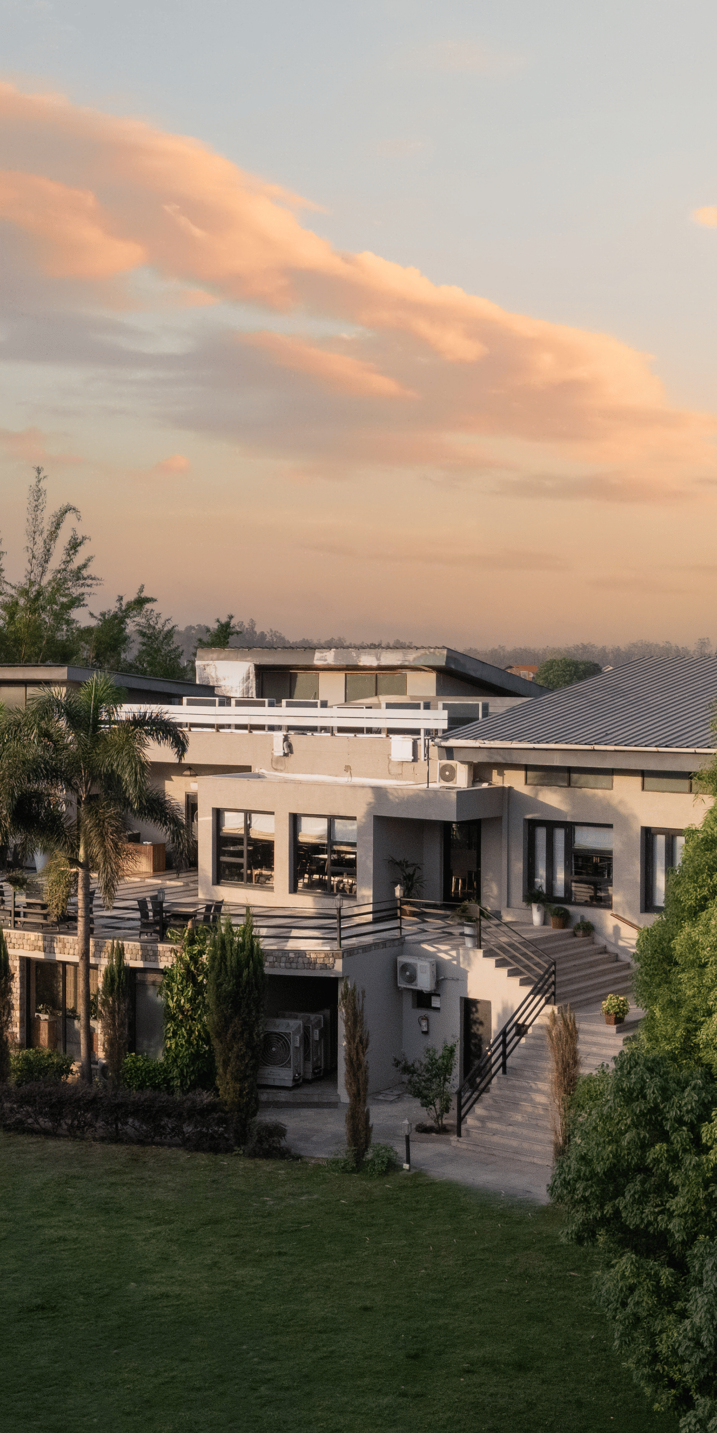 Resort building in the distance, surrounded by green lawns and trees at sunset at The Golden Tusk, Jim Corbett