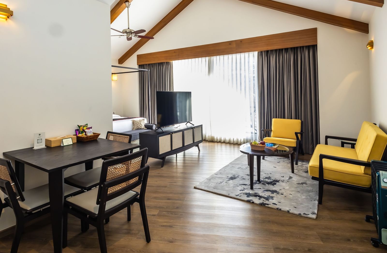 Spacious room with cushioned sofa, wooden table with a TV, and large windows offering scenic nature views at Nivasana Manali.