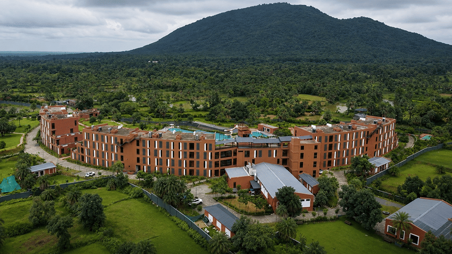 An elevated landscape view of Hotel Sonar Bangla, Susunia featuring brick resort wings, green forest trees, and Susunia Hill in the background.