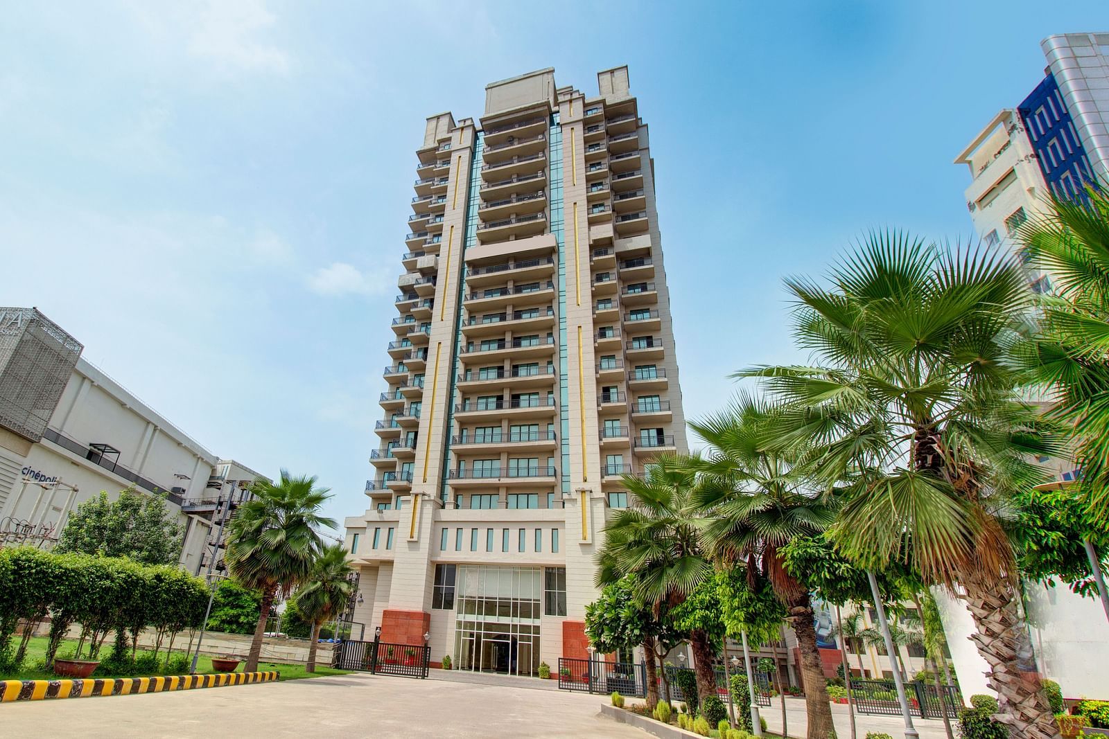 Facade view of the Entrance to Rhythm Gurugram with trees and paved road leading to the hotel.