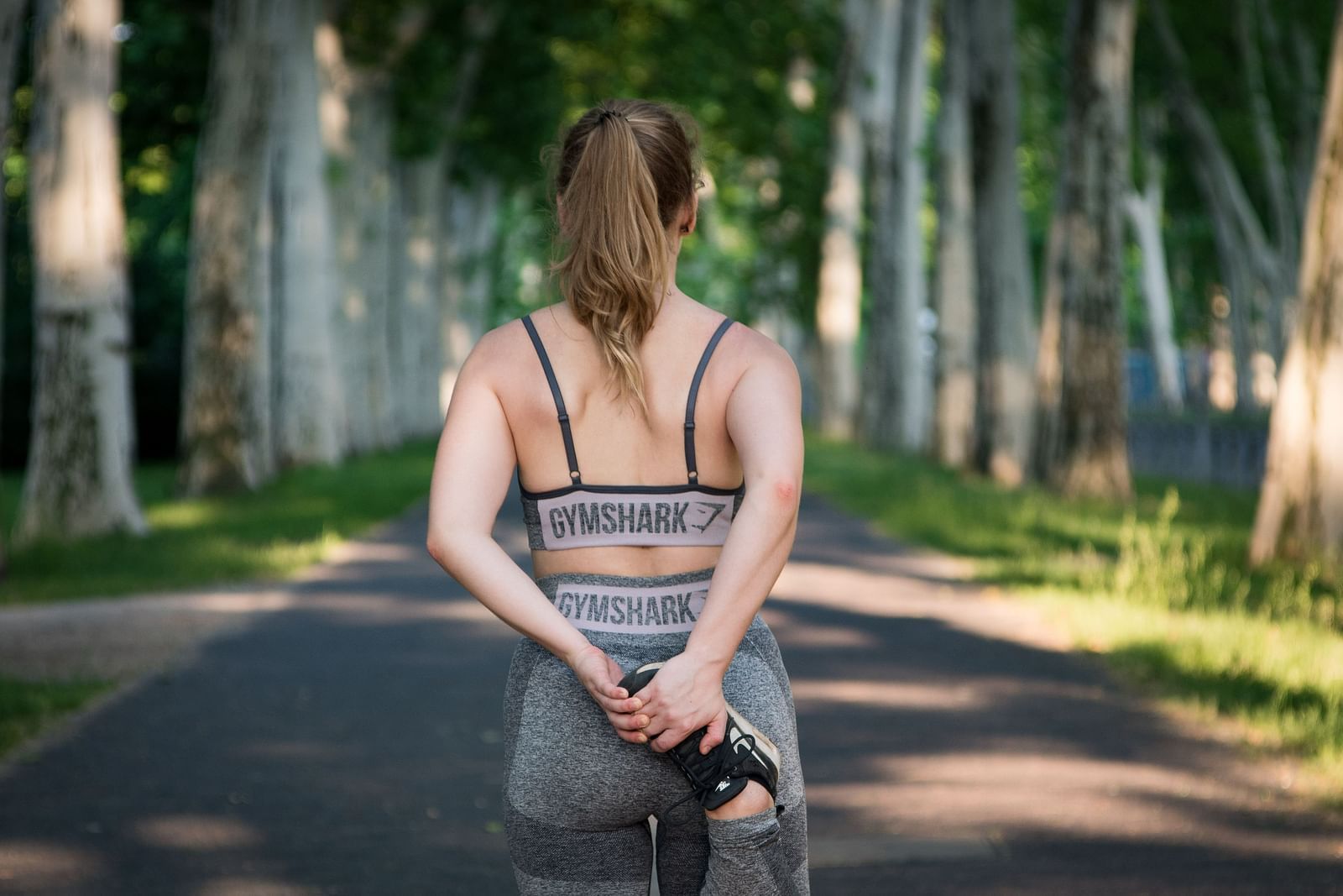 A close up shot of a woman stretching before going on a run on a tarred park road.