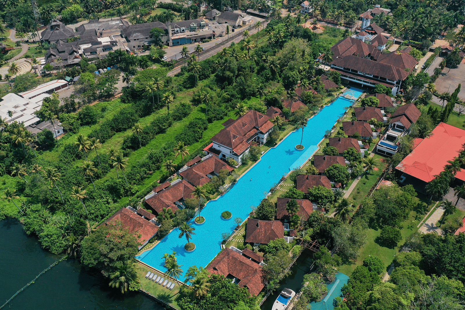 An aerial view of a swimming pool with rooms surrounded by trees - Rhythm Kumarakom
