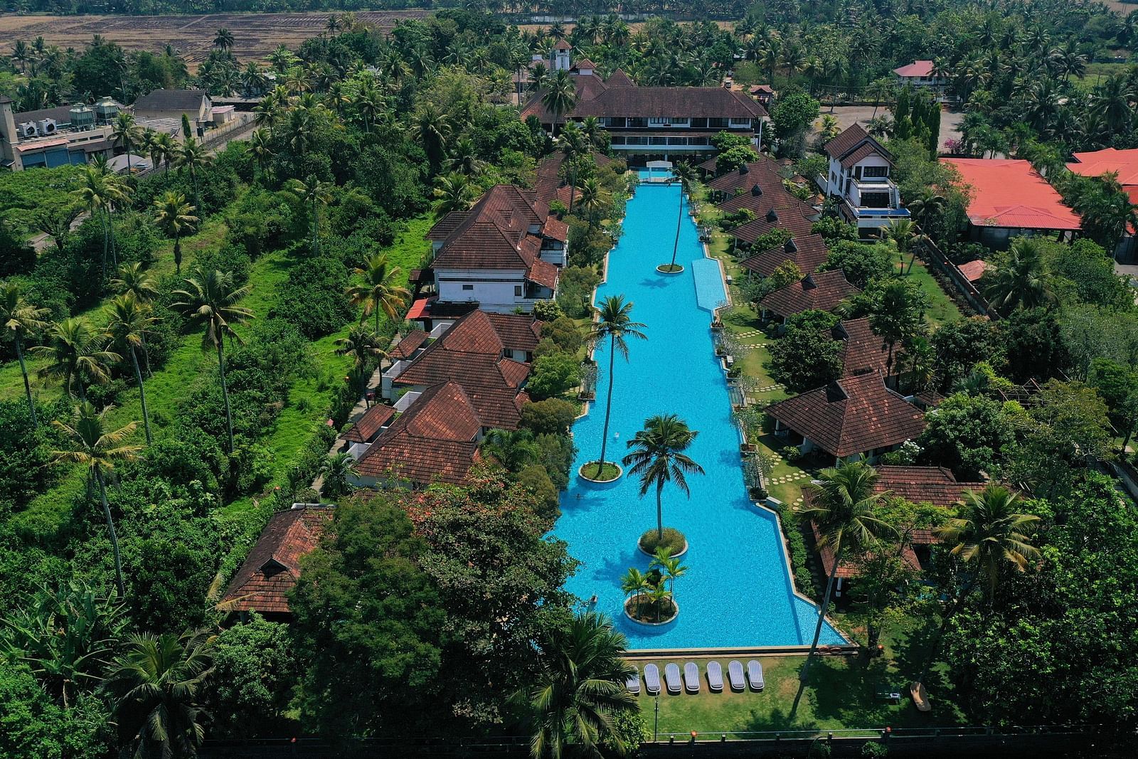An aerial view of india's largest swimming pool with rooms and trees next to it - Rhythm Kumarakom.