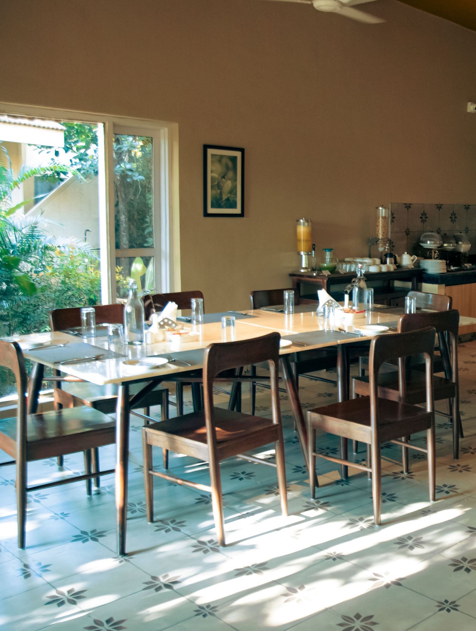 Indoor dining area with neatly arranged tables and chairs, wall decor, and natural light entering through large windows at Fireflies Resorts, Kabini.