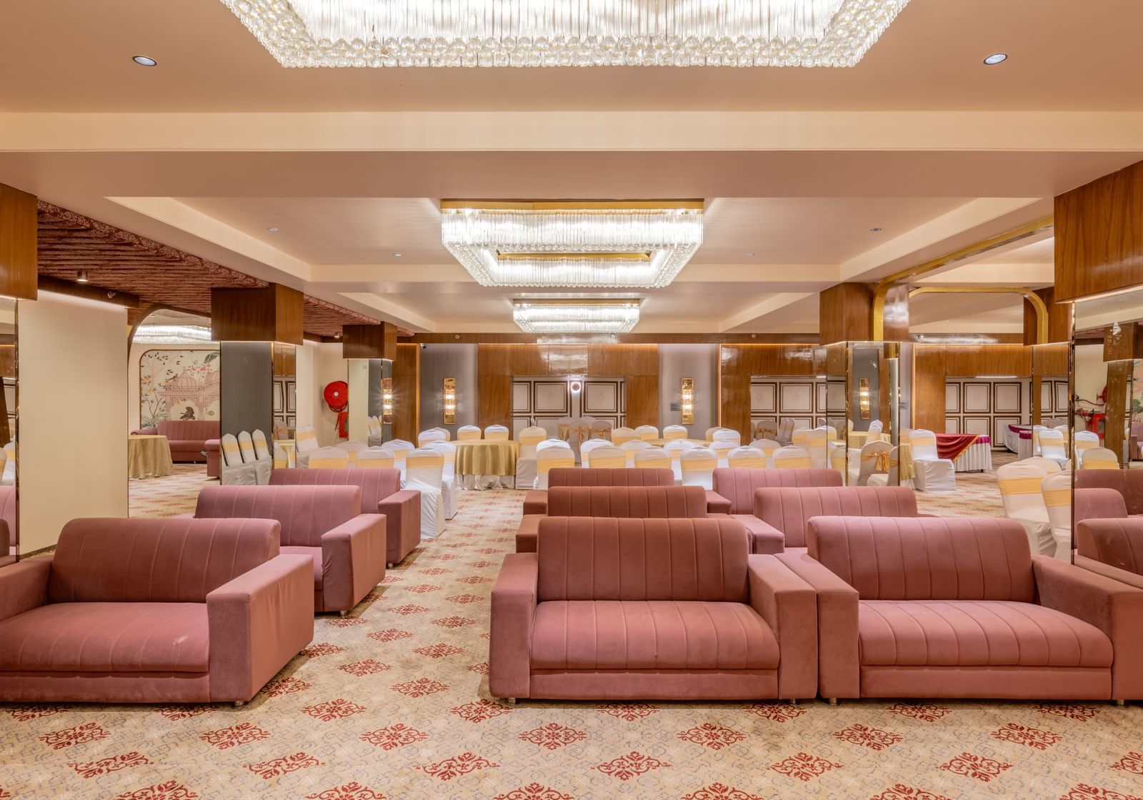 Maroon sofas arranged in a banquet hall with bright ceiling lights above at Hotel Highway King, Jaipur.