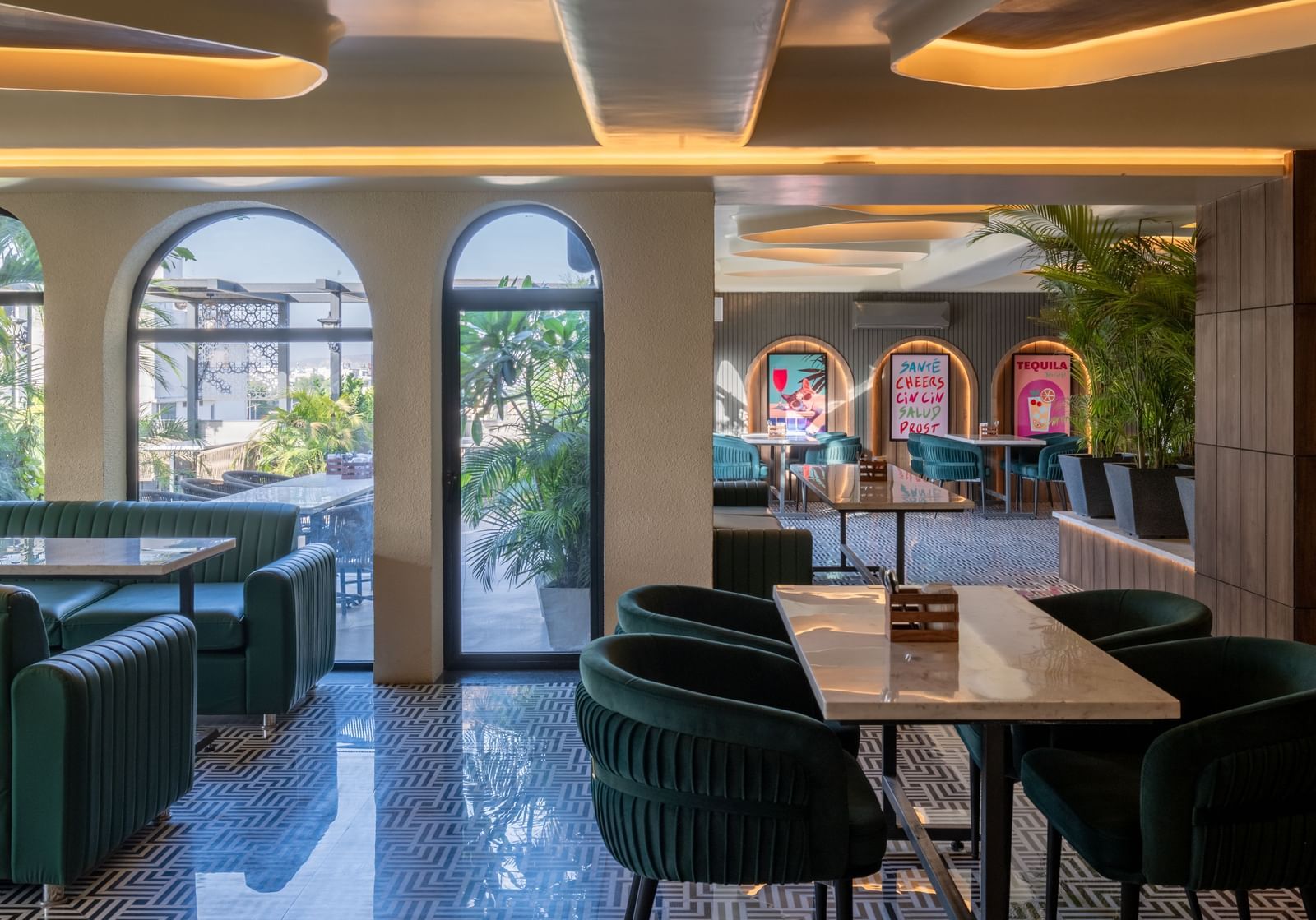 Dining area with green chairs, arched windows, and wall posters at Hotel Highway King, Jaipur.
