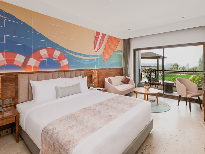 Side view of a bedroom featuring a surf painting above the bed, with a working table and chair at Cloud9 Sarovar Premiere, Palolem Goa.