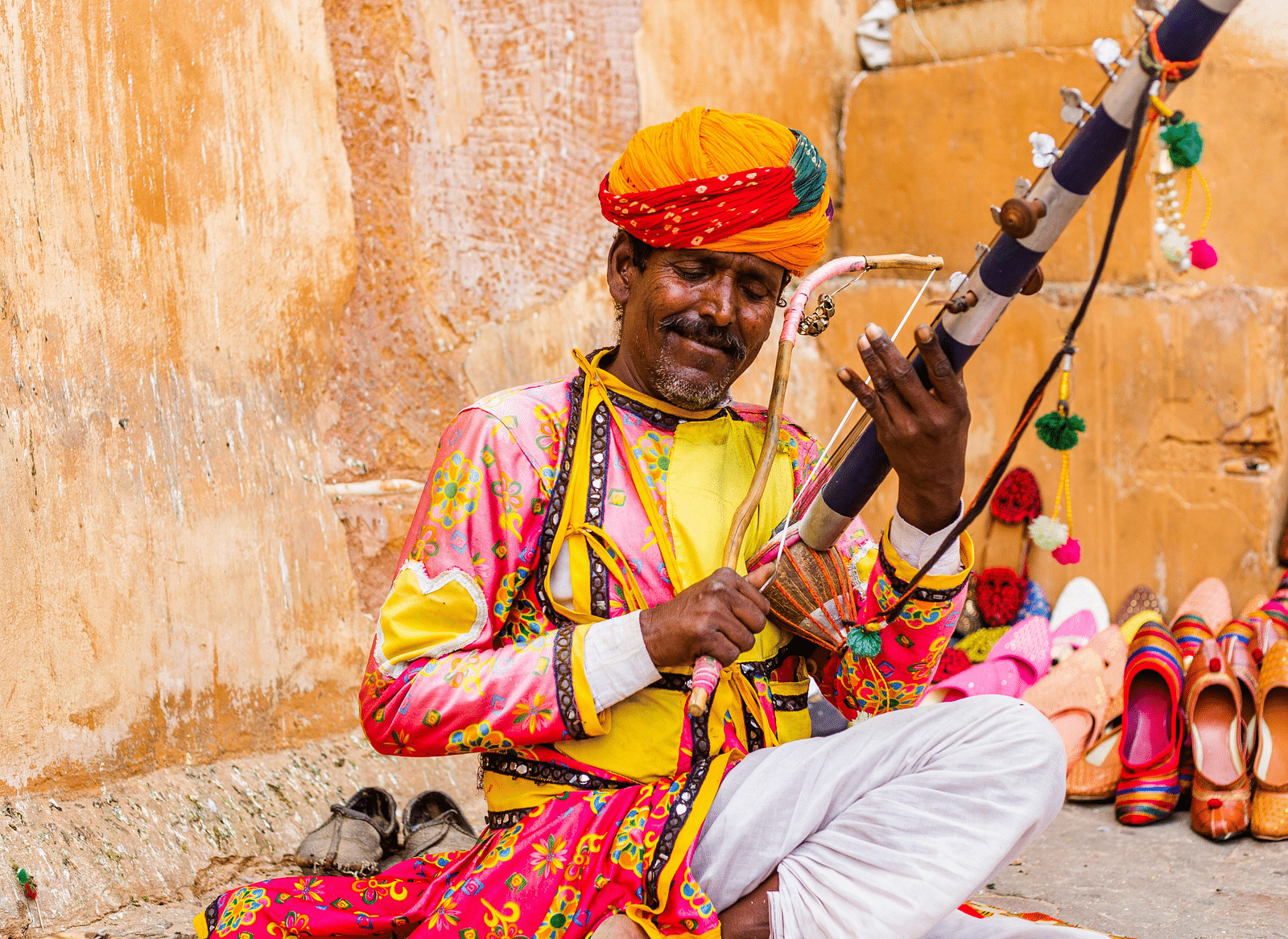 A local musician playing an instrument in front of a tan wall.