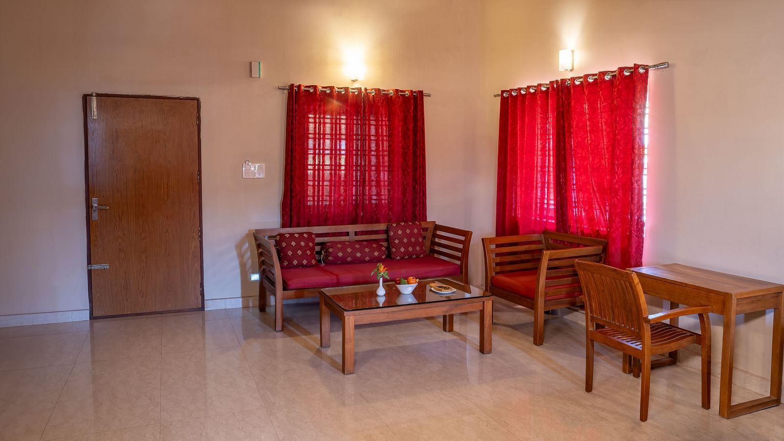 Attic Villa lounge area furnished with wooden chairs, a small table, and red curtains | Woodstock Resorts, Coorg