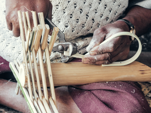 craftsman's dusty hands shaping thin bamboo strips with pliers to weave a traditional item