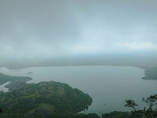 An aerial view of Aliyar Reservoir, surrounded by greenery and mist covering on a gloomy day.