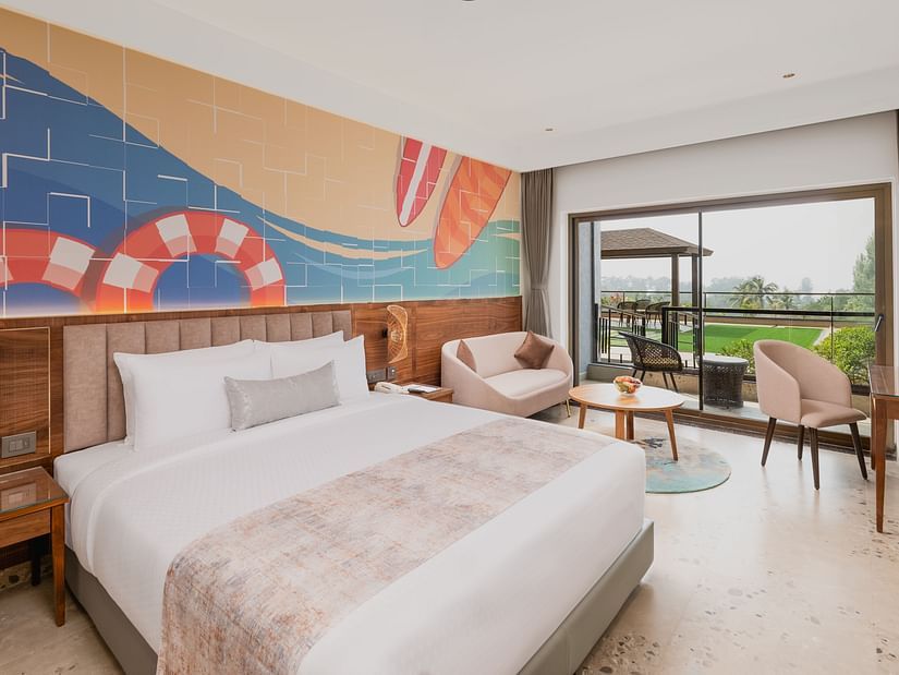 Side view of a bedroom featuring a surf painting above the bed, with a working table and chair at Cloud9 Sarovar Premiere, Palolem Goa.