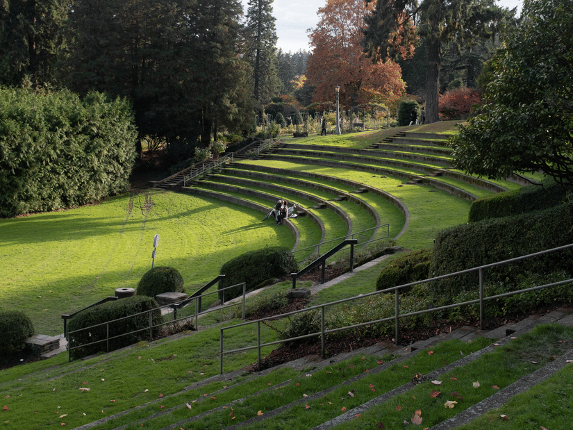 Terraced outdoor amphitheatre in a lush green park with curved seating steps, surrounded by trees and autumn foliage.
