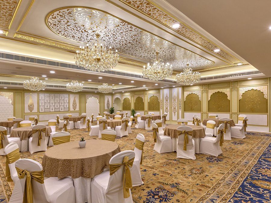 Lavish ballroom with ornate ceiling, multiple chandeliers, and round tables with white and gold accents - Heritage Village Resorts & Spa.