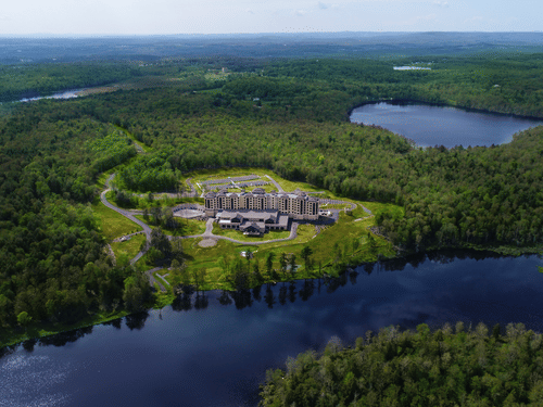 Exterior view of YO1, Catskills, New York, showcasing its modern facade surrounded by lush greenery and a lake.