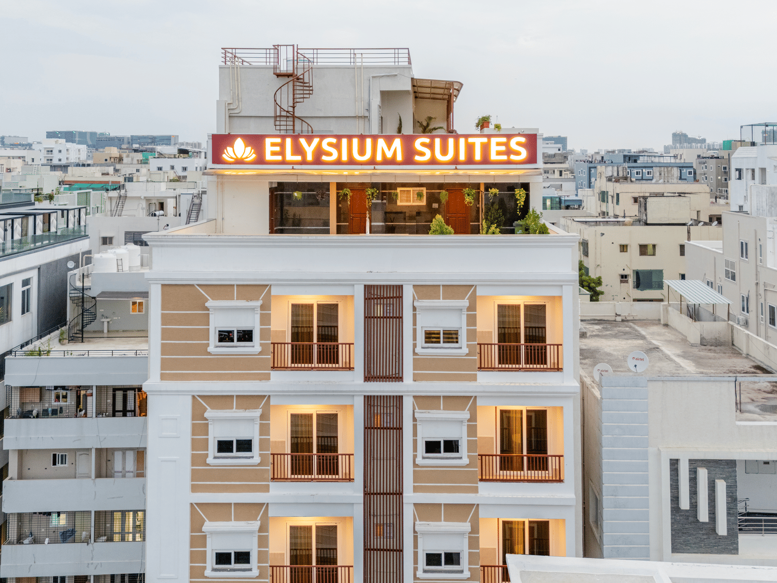 The exterior of Elysium Studio Suites, Madhapur, shows a multi-storey building with balconies under a cloudy sky.