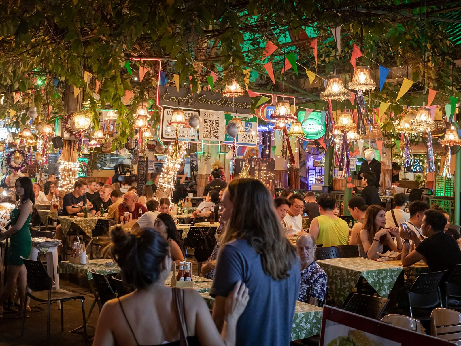 people walking and sitting in a crowded seating area with restaurants in the background 