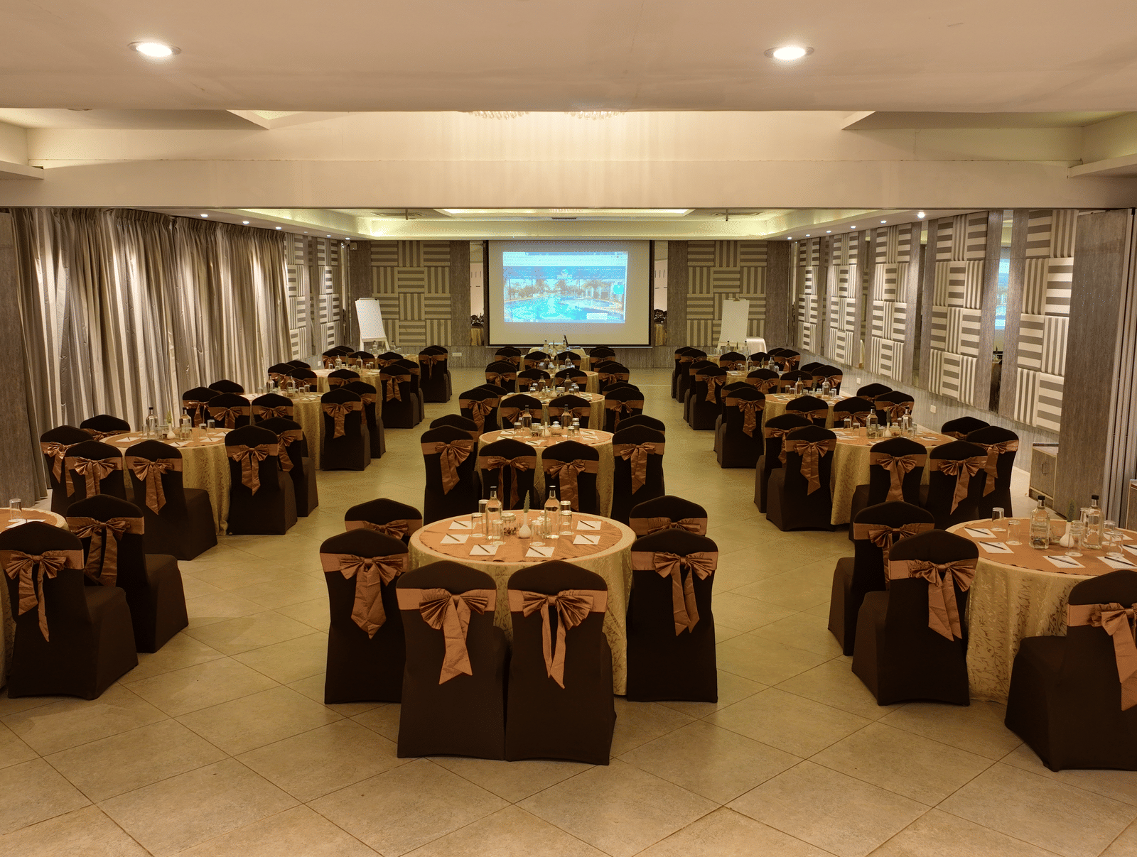 Banquet hall with brown chair covers arranged around round tables at Grande Bay Resort & Spa, Mamallapuram.