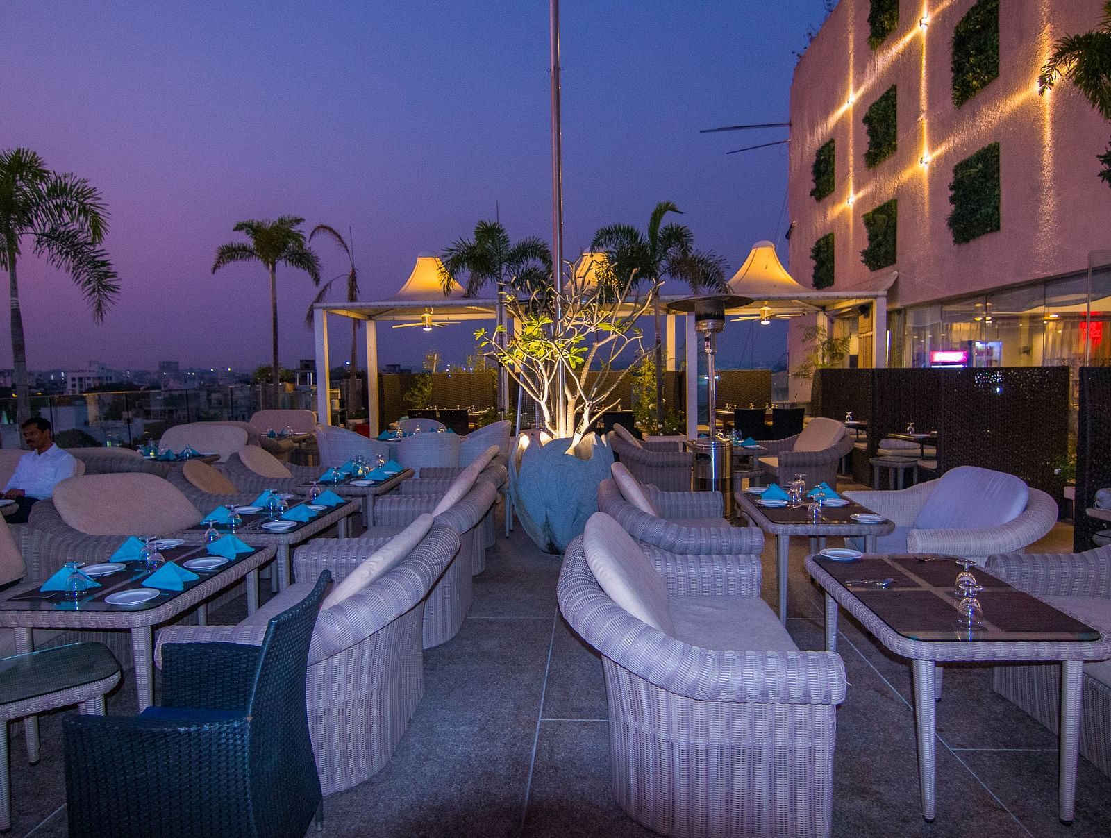An outdoor dining setup at Hotel Ashok Nagpur with white cushioned chairs and small tables arranged for guests.