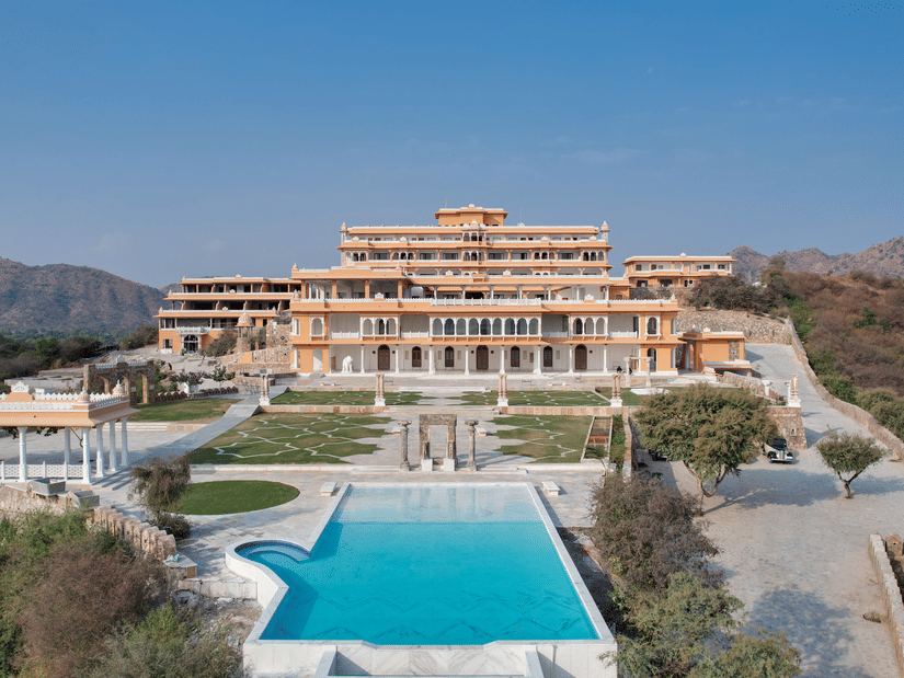 View of Fateh Vilas, Udaipur with a swimming pool in front of the property surrounded by the mountains.