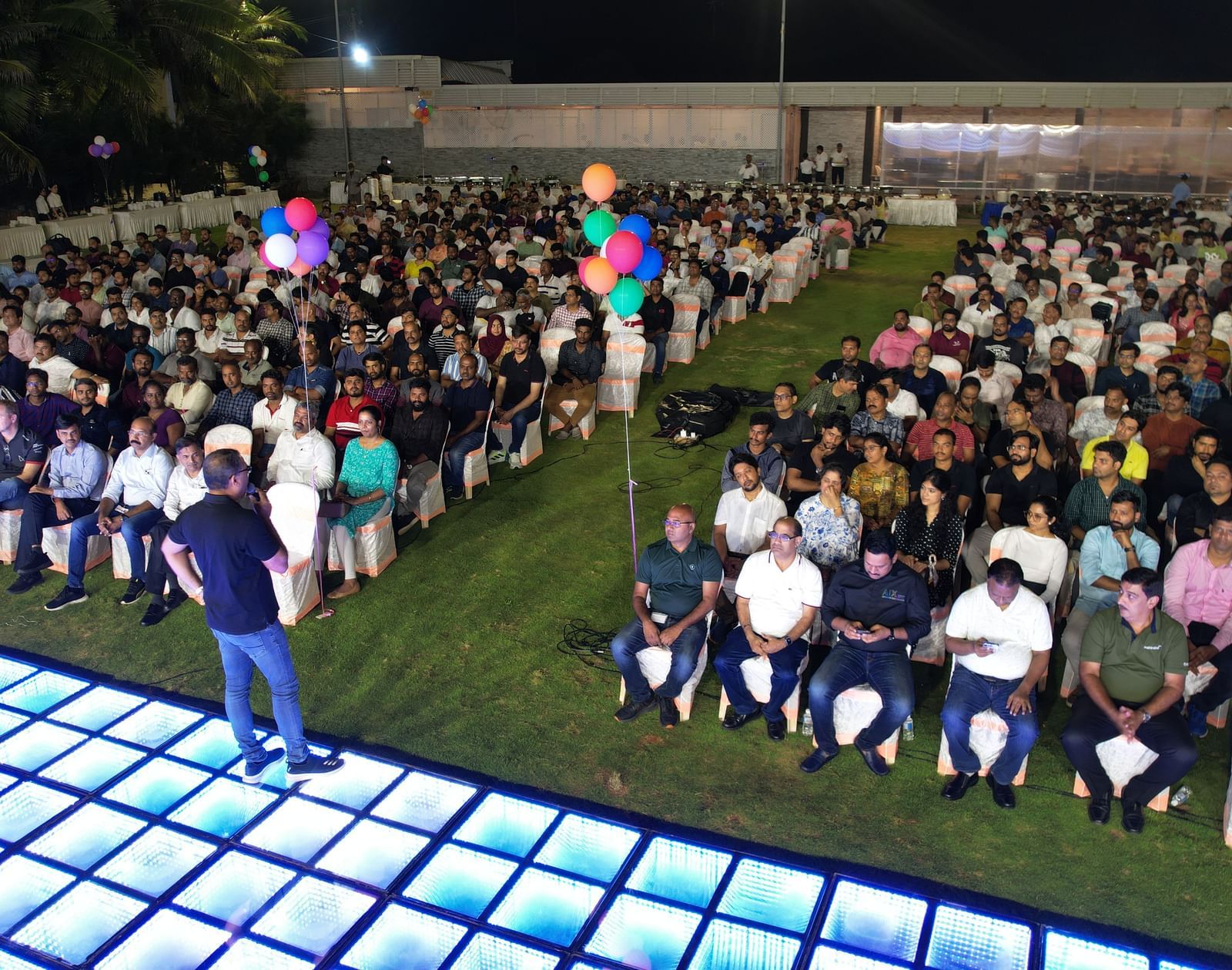 An outdoor corporate event held at Grande Bay Resort & Spa featuring people seated in chairs and a person on a grid structured stage.