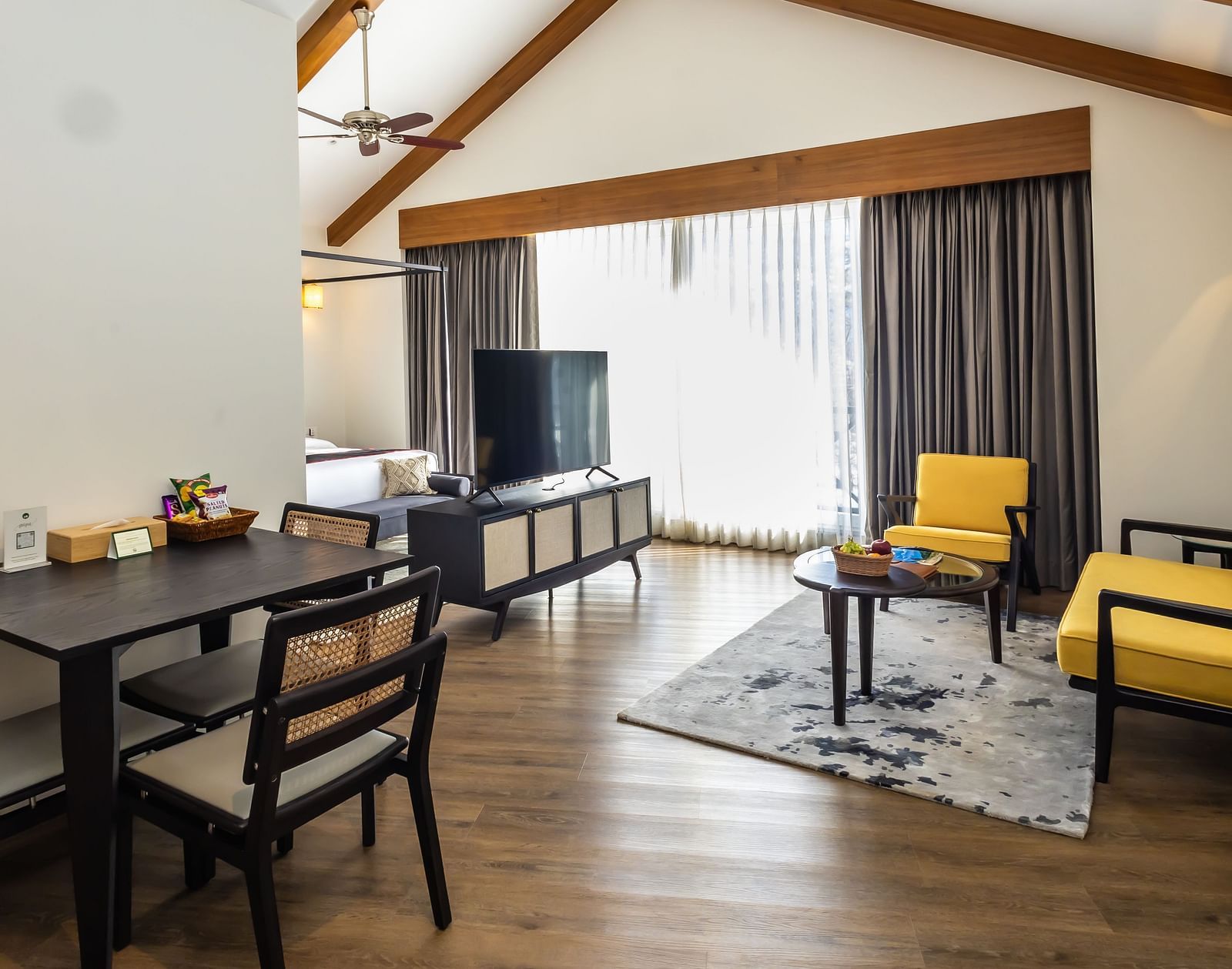 Spacious room with cushioned sofa, wooden table with a TV, and large windows offering scenic nature views at Nivasana Manali.