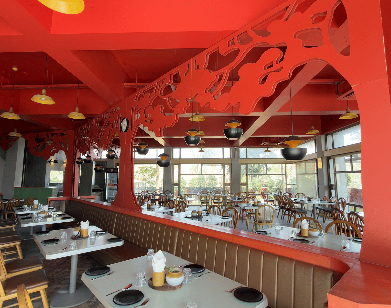 The restaurant at Vinti Resort, Ambaji, lit for meals, features a striking pink ceiling and comfortable tables set for dining.